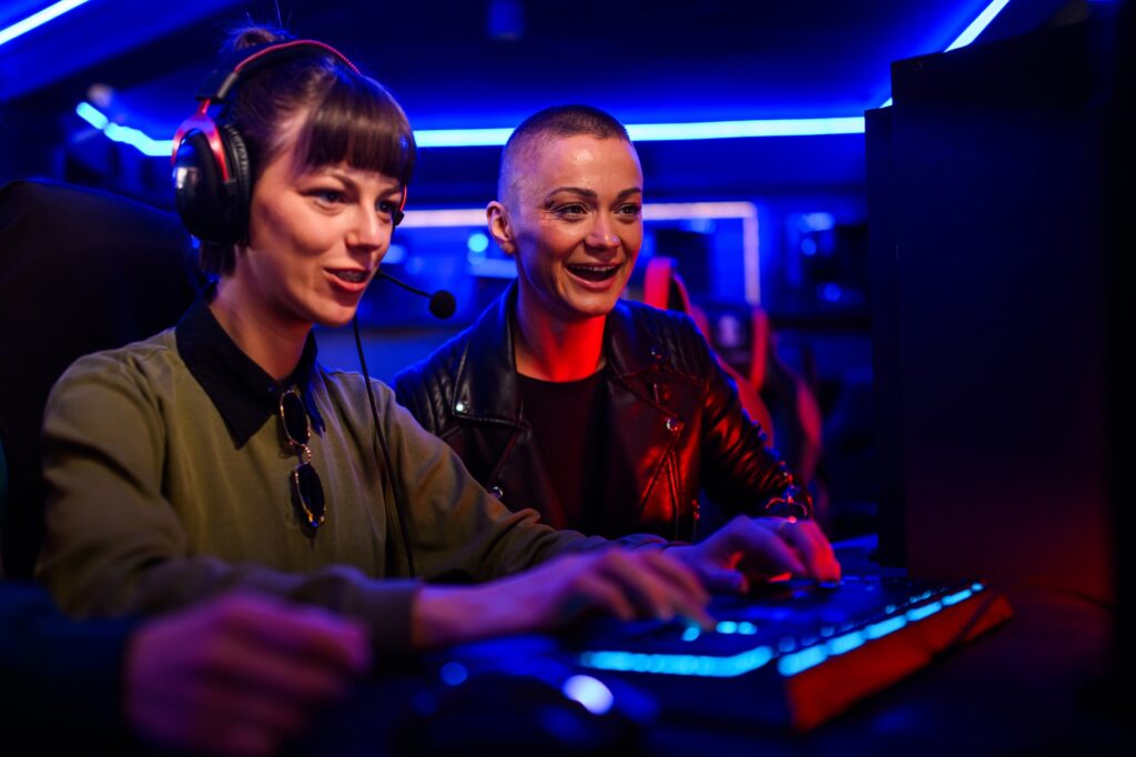 Gamer girl playing a game in cybercafe while her friend is cheering.